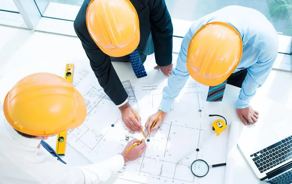 Engenheiros com capacetes laranja analisando planta sobre a mesa